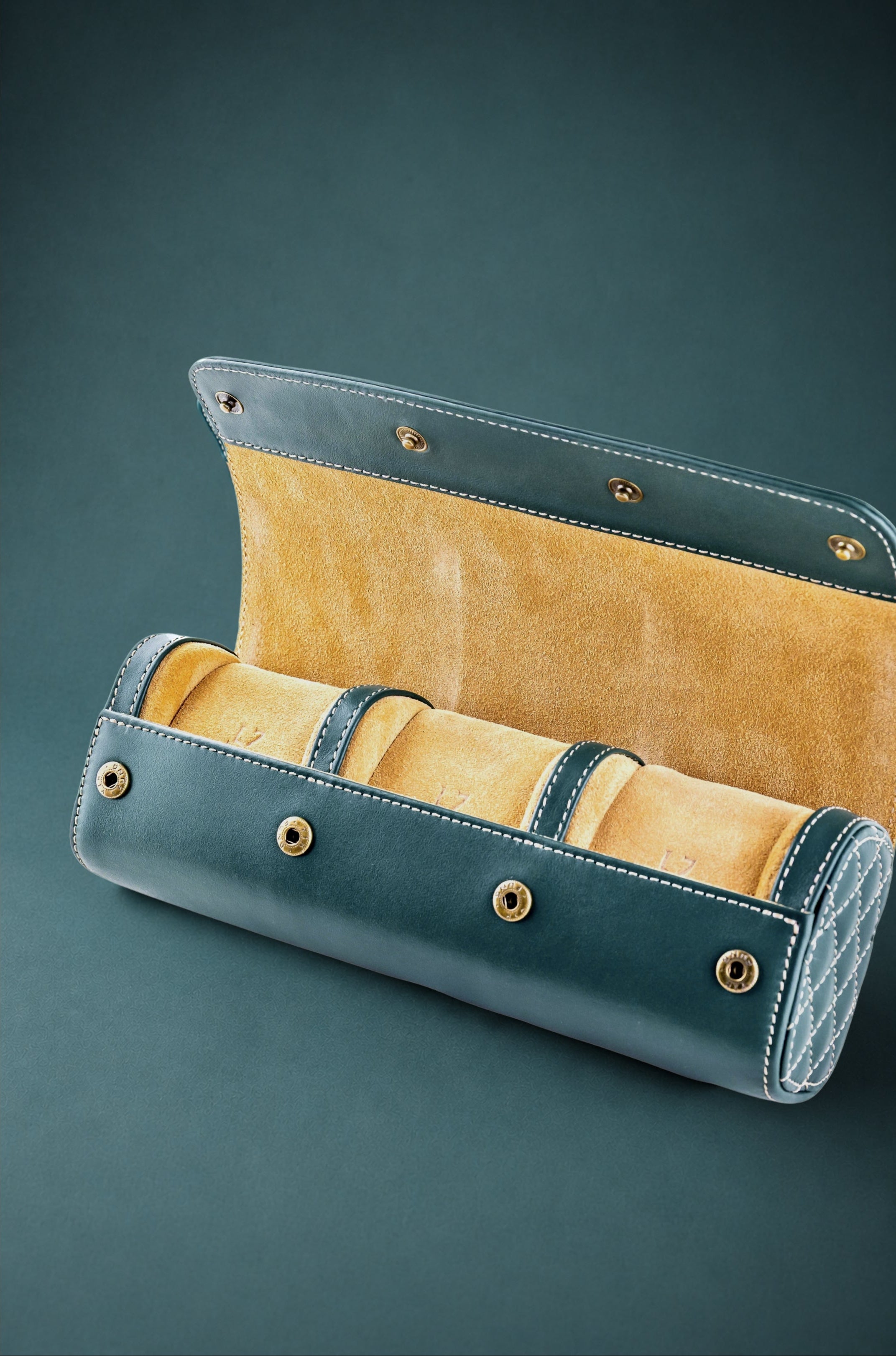 British racing green watch roll with mustard interior containing three watches on a dark green background