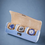 Three watches in a light blue and beige display case on a gray background