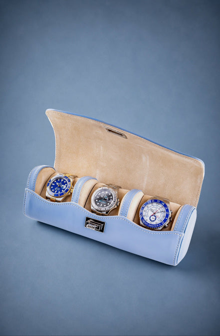 Three watches in a light blue and beige display case on a gray background