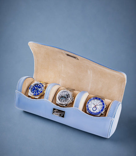 Three watches in a light blue and beige display case on a gray background